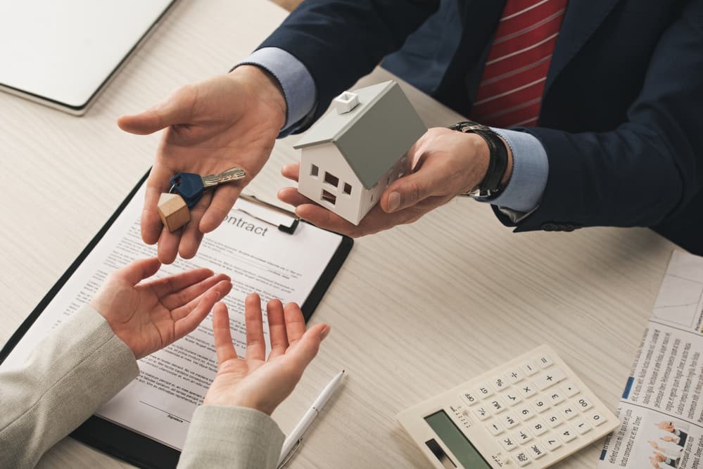 Man handing keys and a toy home to another person