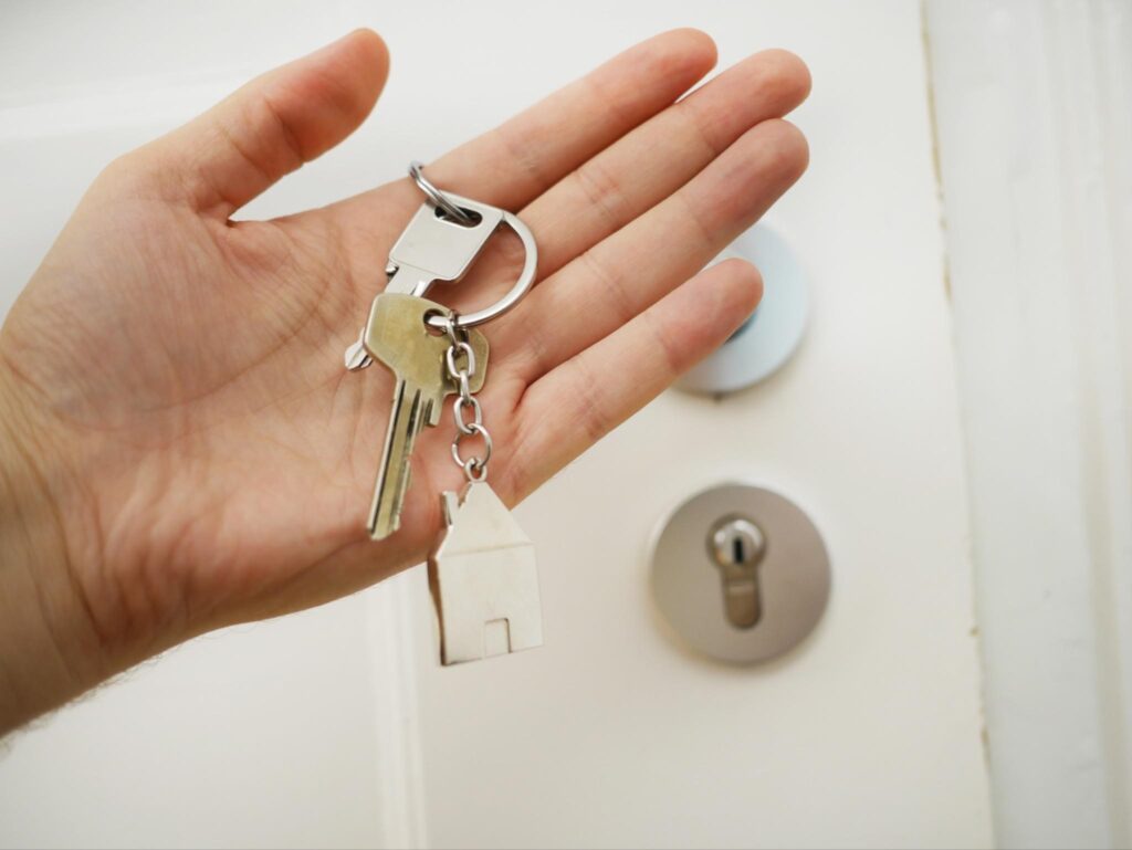 A hand holding house keys with a door behind. 